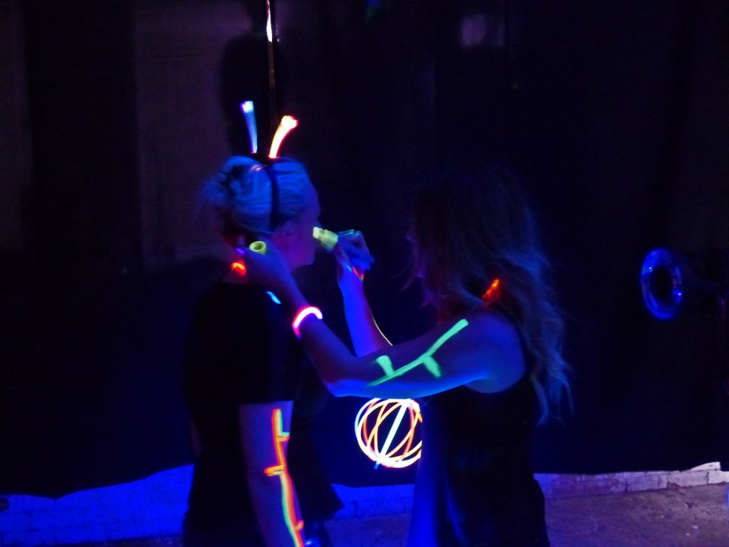 Mädchen mit im Schwarzlicht leuchtenden Schmuck bemalen sich mit Schwarzlichtstiften